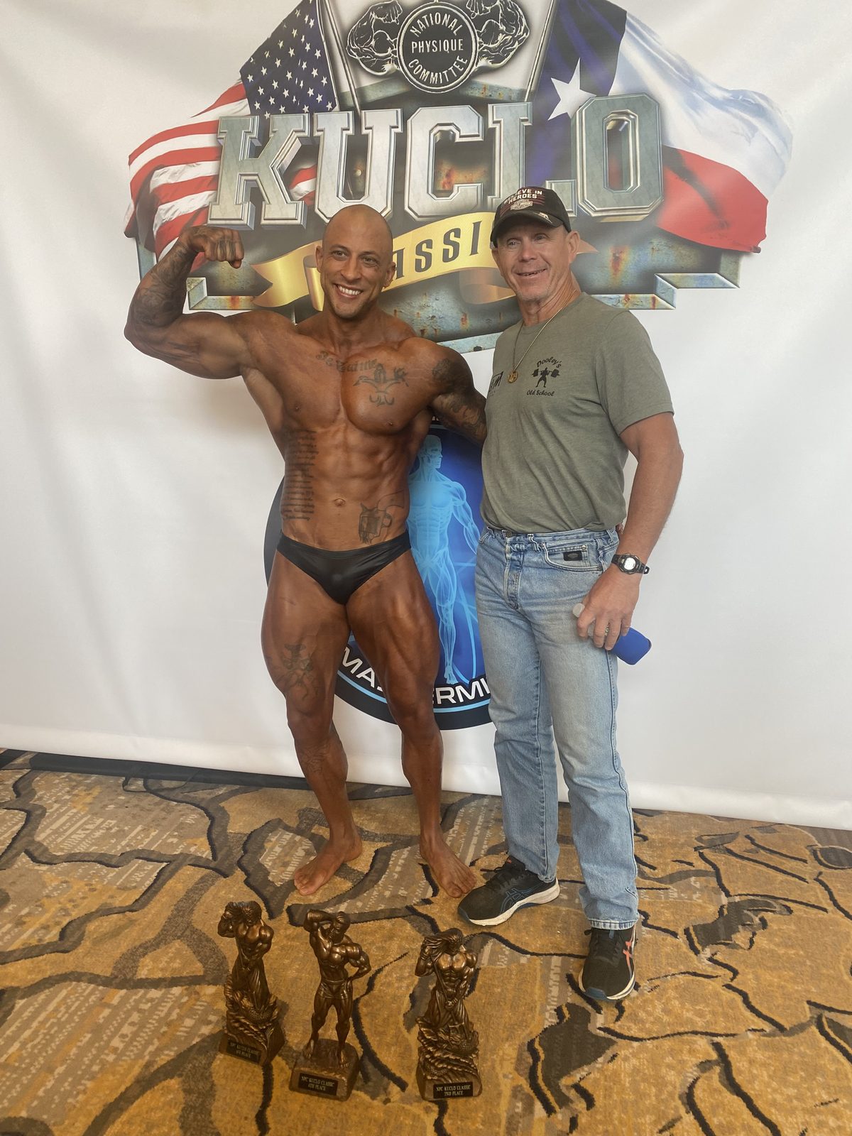 A bodybuilding competitor and Jim Dooley standing with trophies
