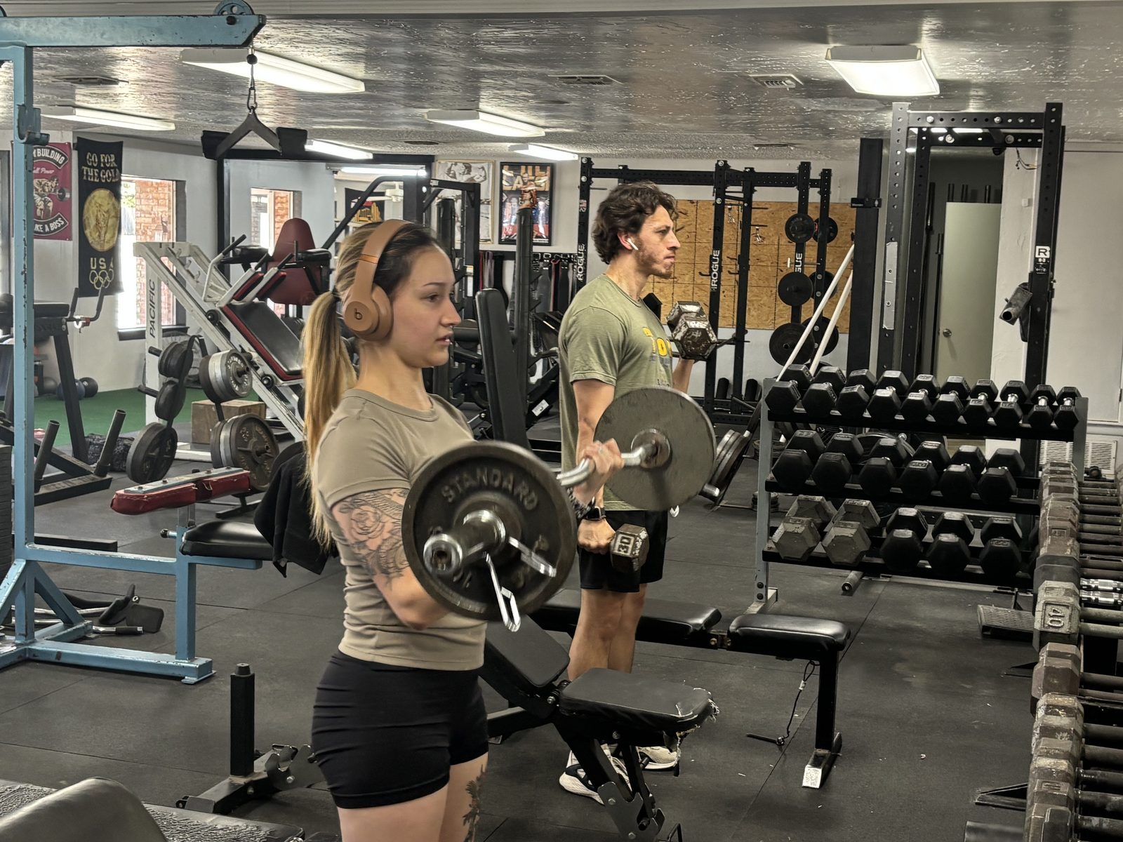 Two members training arms with a barbell and dumbbells