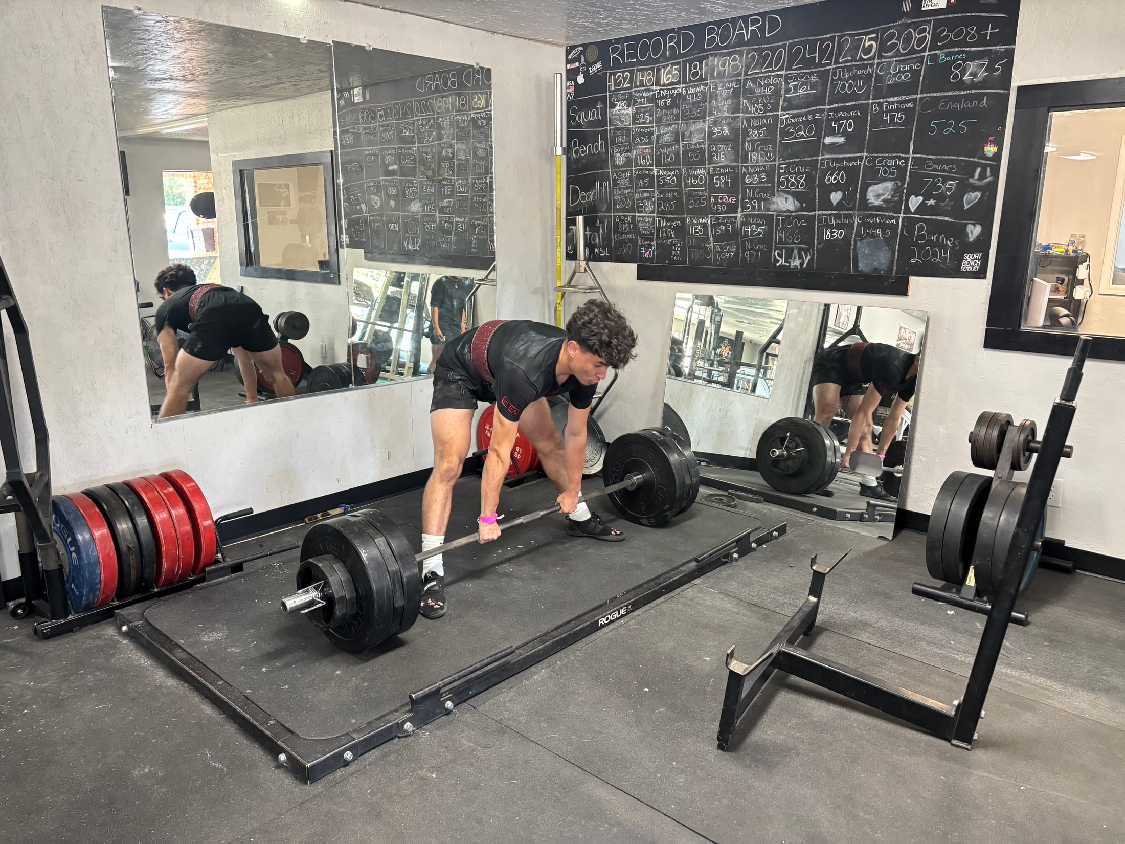 A member setting up for a deadlift beneath the gym record board