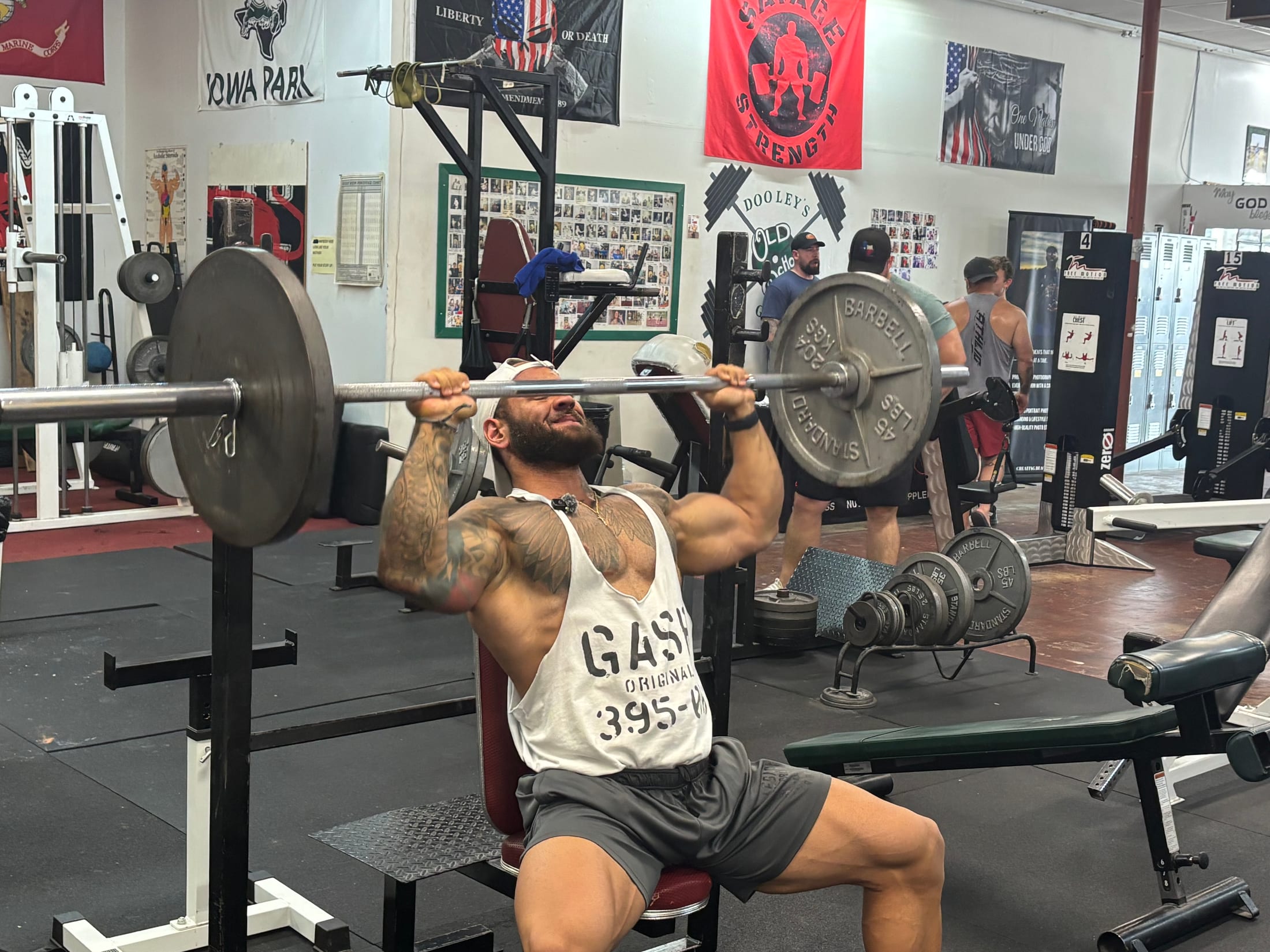 A member performing a seated barbell overhead press